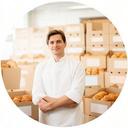 Portrait einer Bäckerei-Leiterin in einer hellen Backstube mit frisch gefüllten Kartons